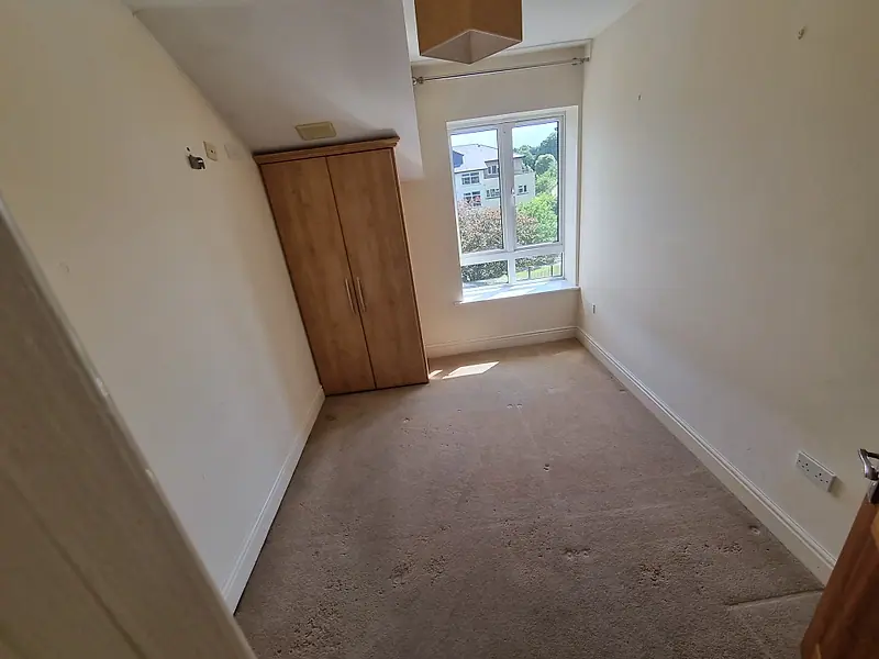Empty carpeted apartment bedroom with fitted wardrobe after clearance