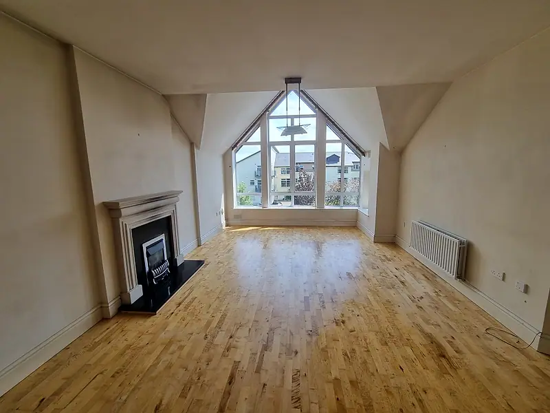 The same apartment living room after clearance, empty with the oak floor and gable window showing