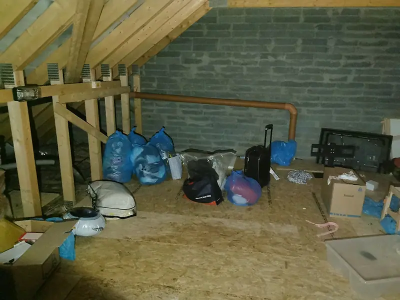 Attic in a Dublin house before clearance, with bags, a suitcase and boxes on the boarded floor