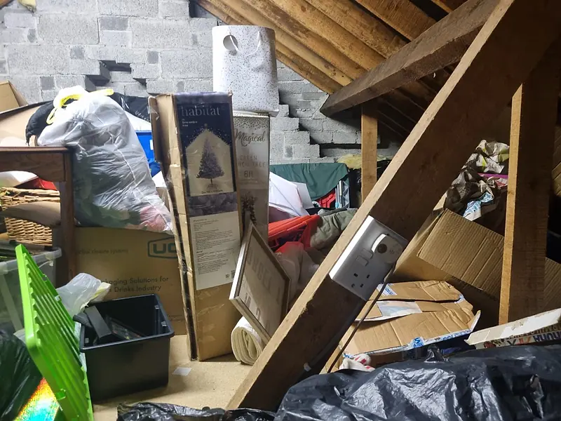 Attic packed with boxes and bags beside a blockwork gable wall before clearance