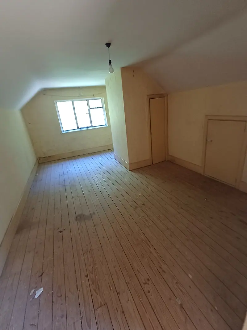 Cleared attic conversion room with bare pine floorboards and a dormer window