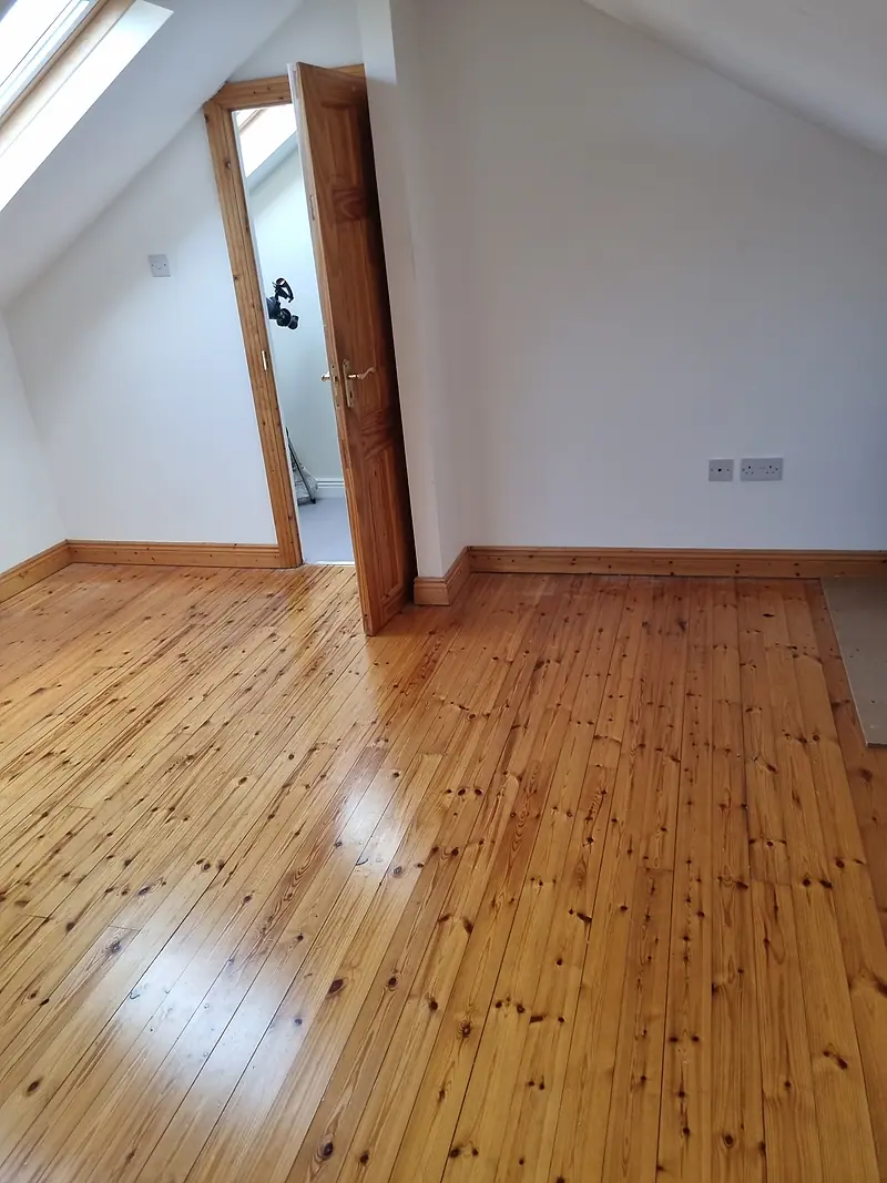 The same attic room empty after clearance, pine floor and open door