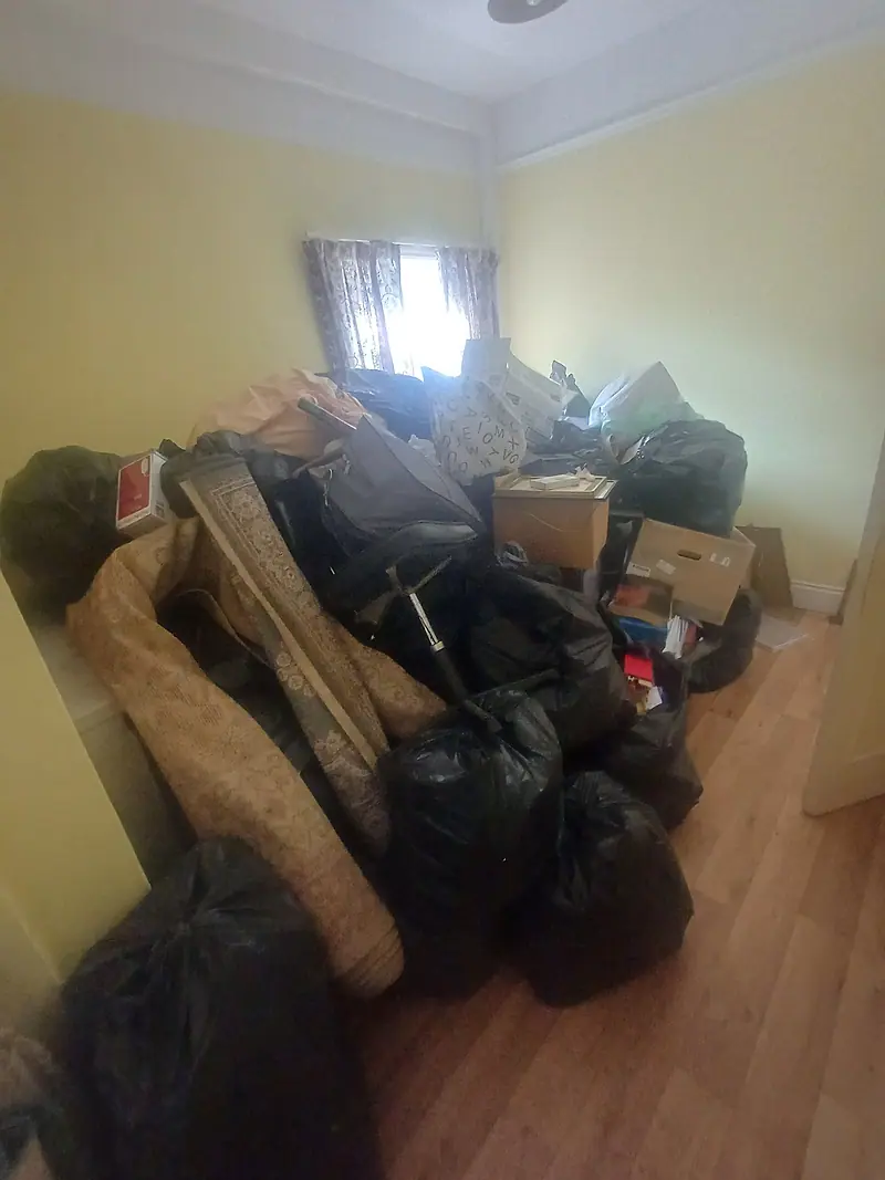 Bedroom piled high with black bags, boxes and rolled rugs before clearance
