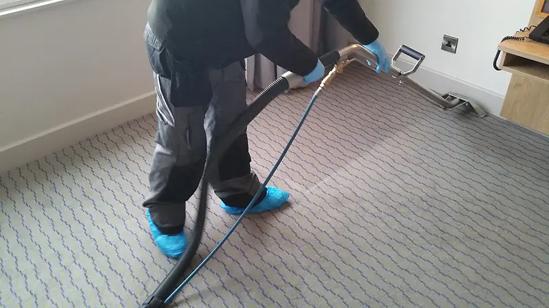 Technician in shoe covers cleaning a patterned carpet with a hot-water extraction wand
