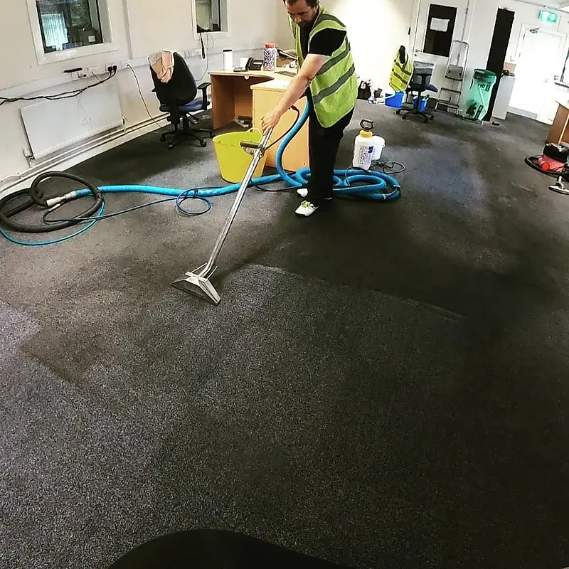 Office carpet being cleaned between desks with a hot-water extraction machine