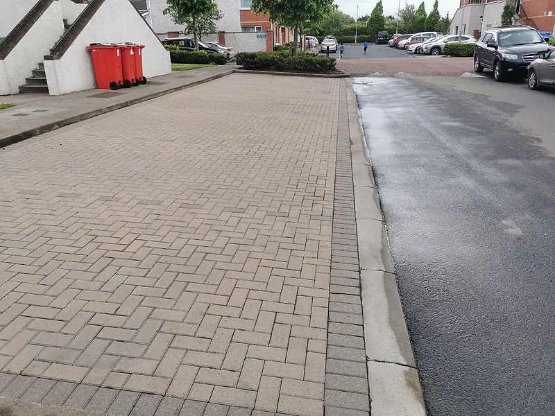 Block-paved driveway part-way through power washing, the cleaned strip clearly lighter than the untouched paving
