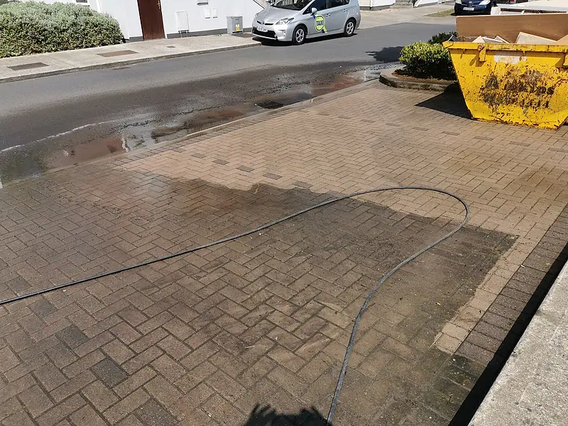 Driveway being power washed, the hose across the paving and a clean section already finished