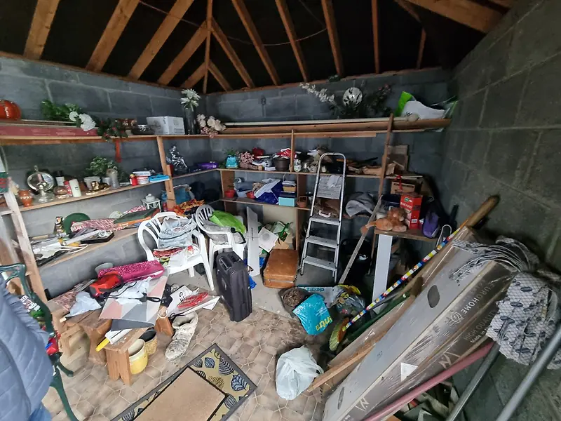 Garage with shelves, garden chairs and boxes piled up before clearance