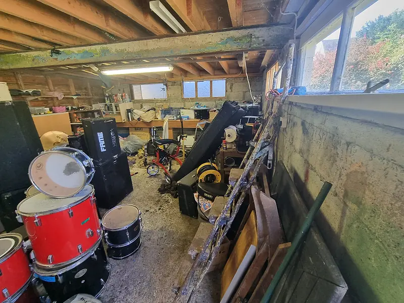 Garage with a drum kit, speakers and tools waiting to be cleared