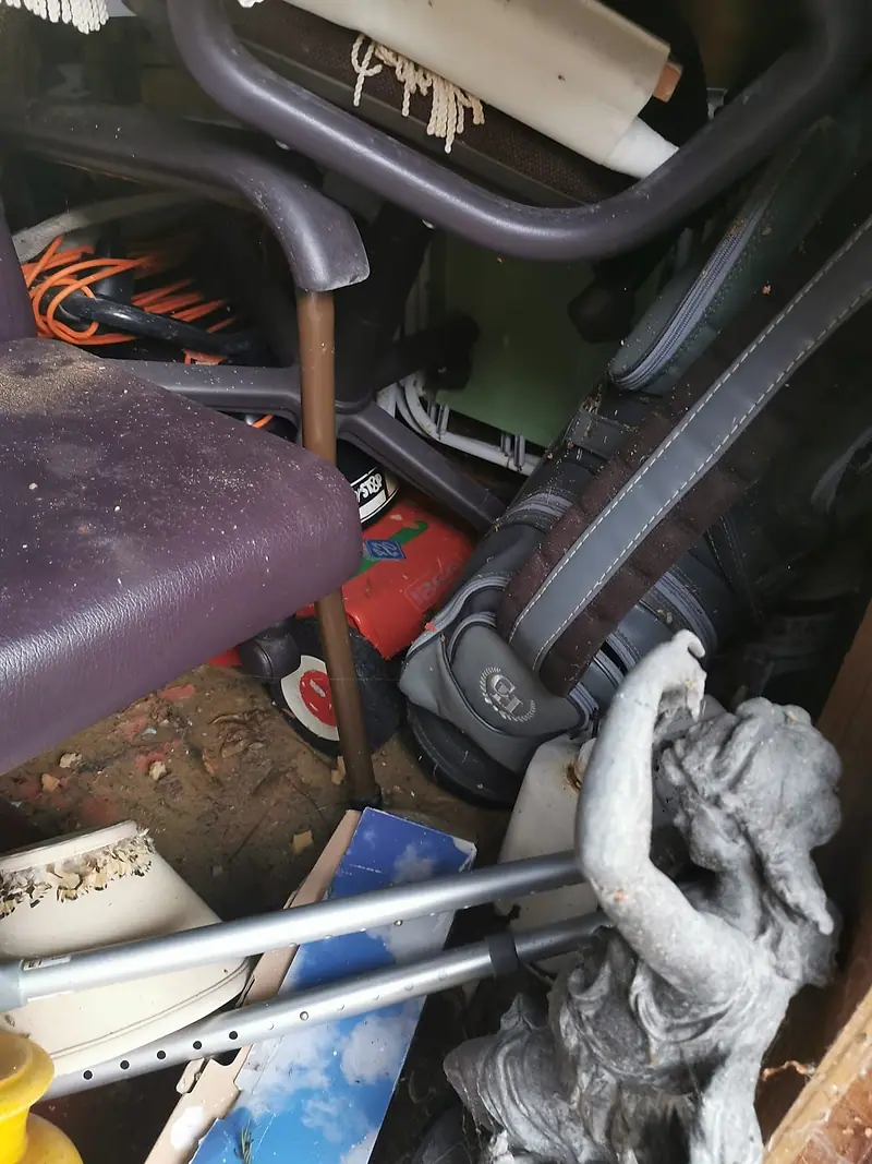 Mixed junk in a garage, including an old chair, a vacuum cleaner and a garden ornament