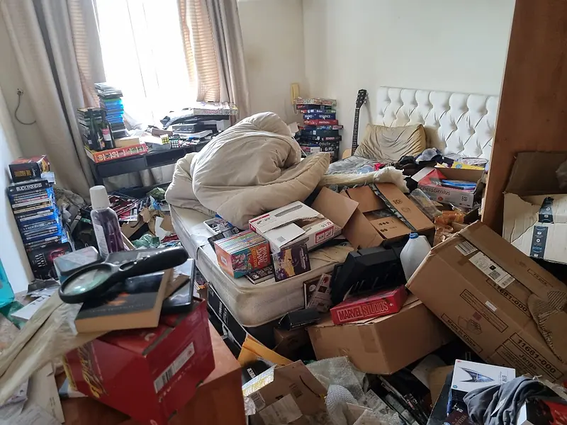 Bedroom piled with boxes, bedding and clutter before a careful clearance