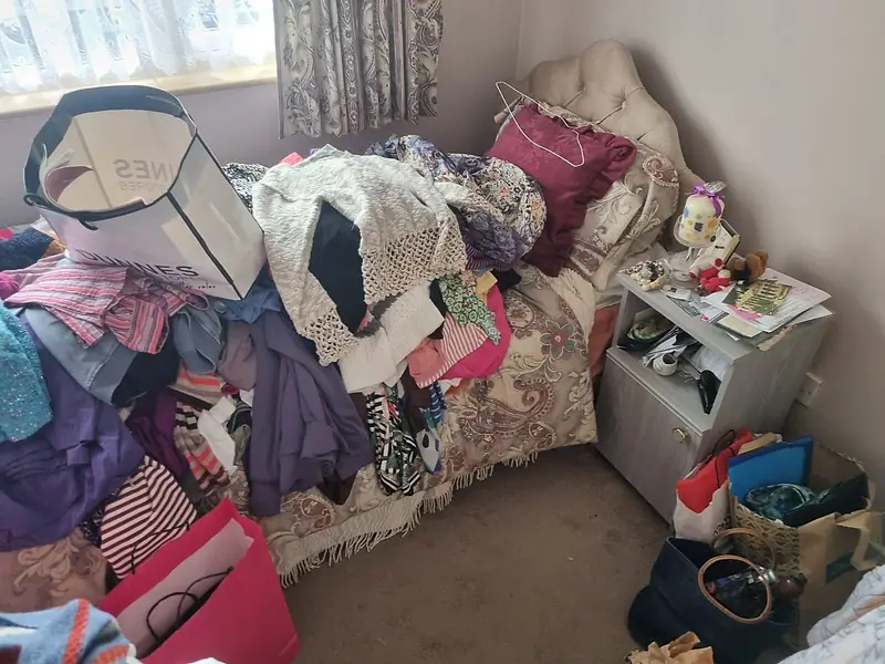 Bedroom piled with clothes and bags before a careful, staged clearance