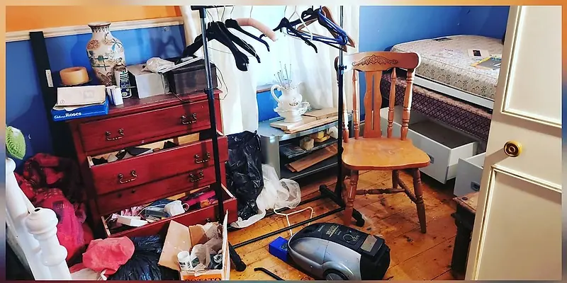 Bedroom with a chest of drawers, chair and belongings spread on the floor before clearance