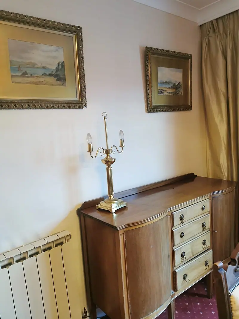 Wooden sideboard with a brass lamp and framed pictures in a house being cleared