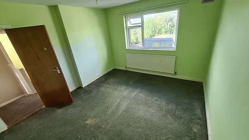 The same back bedroom after clearance, empty with green walls and carpet