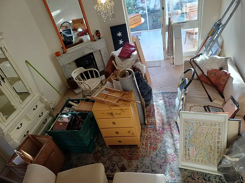 Living room crowded with furniture, boxes and pictures before a full house clearance