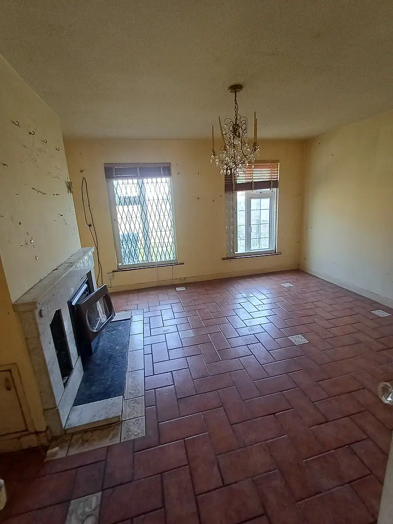 Empty living room with a marble fireplace and terracotta tiled floor after clearance