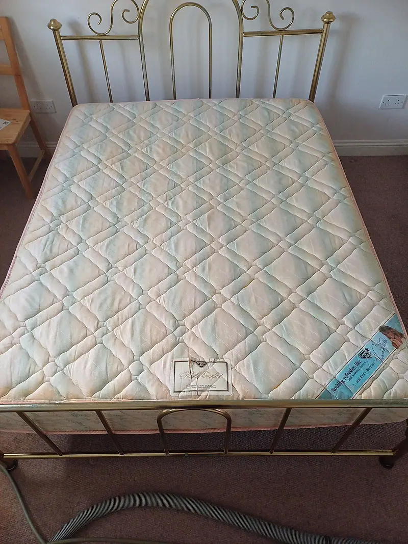 Quilted double mattress on a brass bed frame with the extraction hose in view