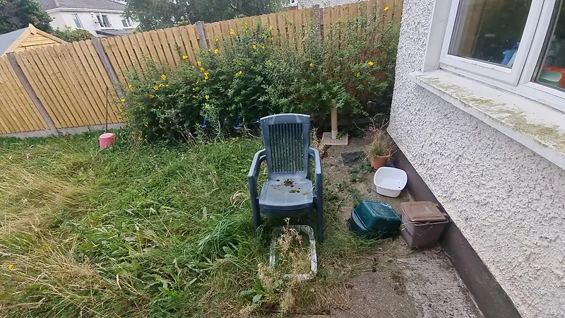 Overgrown back garden with an old plastic chair and discarded items before clearance