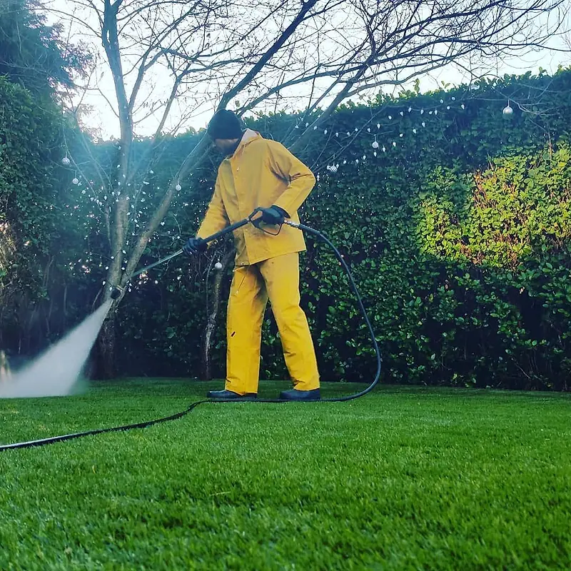 Spotless operative in waterproofs power washing in a back garden