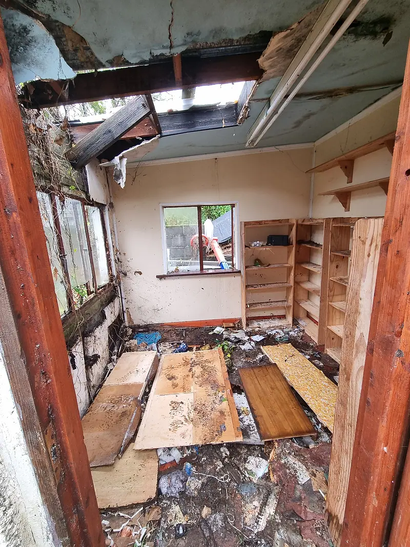 The same outbuilding emptied, with bare shelving and boards on the floor