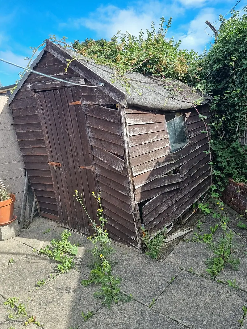 Dilapidated timber garden shed with a sagging roof, ready to be taken down
