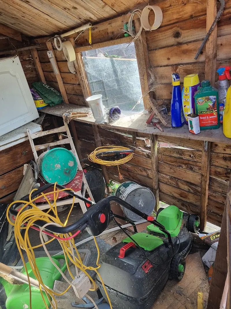 Shed interior crammed with a lawnmower, hoses, tools and garden products