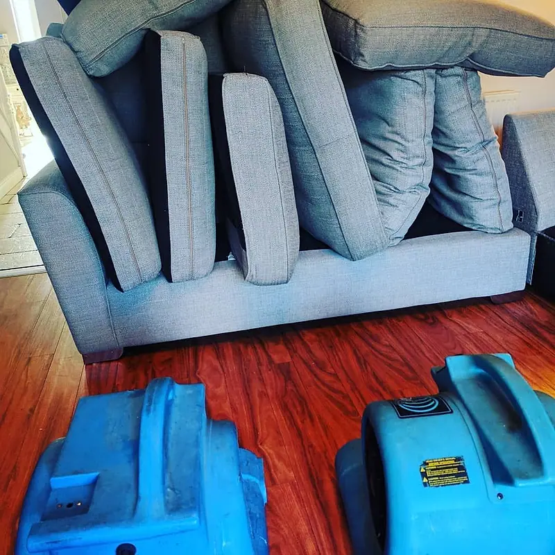 Grey sofa with cushions lifted to dry beside two air movers