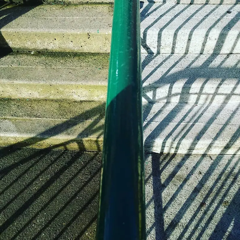 Concrete steps with a green handrail, dark with algae before cleaning