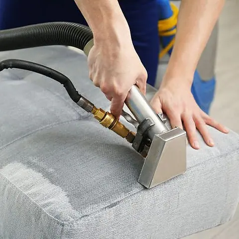Upholstery tool cleaning a grey fabric sofa, the cleaned stripe visible