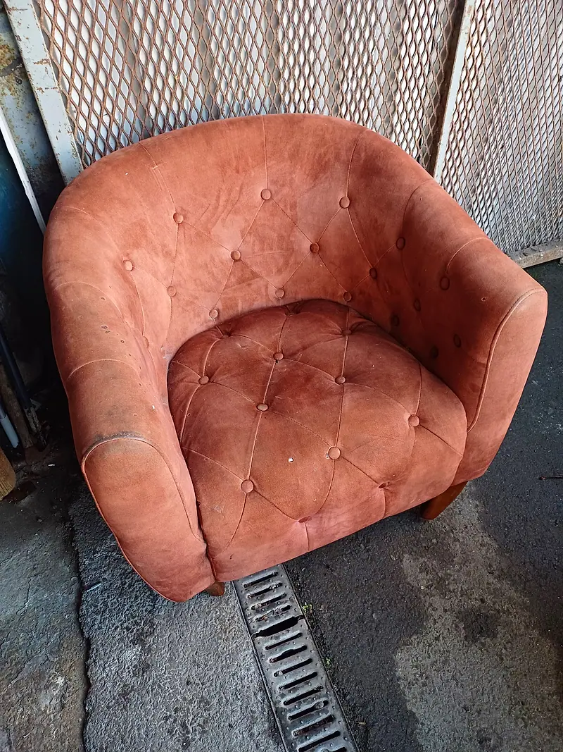 Heavily soiled orange velvet tub chair with a buttoned back before cleaning