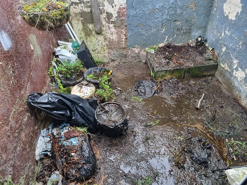 Small back yard with bags of garden waste, pots and debris before clearance